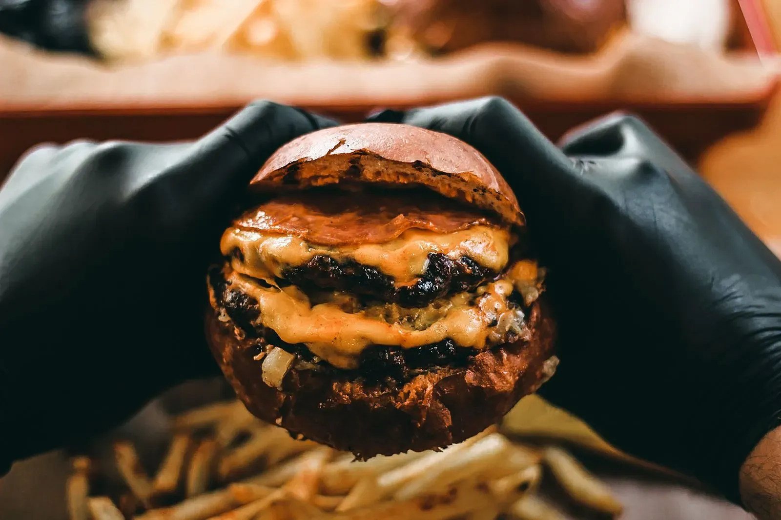 Burger double patty dengan keju leleh dipegang tangan bersarung